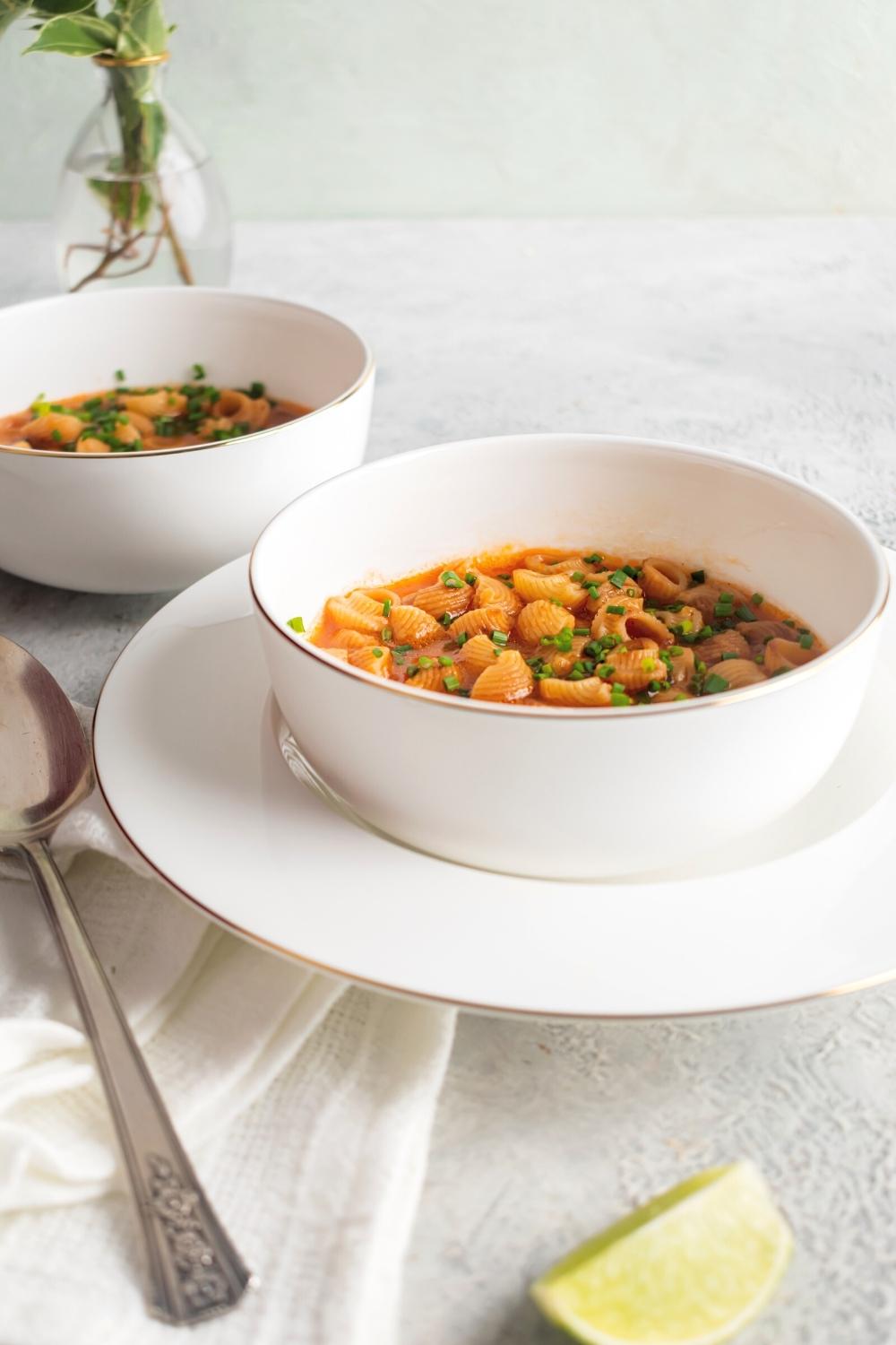 A white bowl filled with Mexican soup on top of a white plate. Behind it is another white bowl filled with the soup.