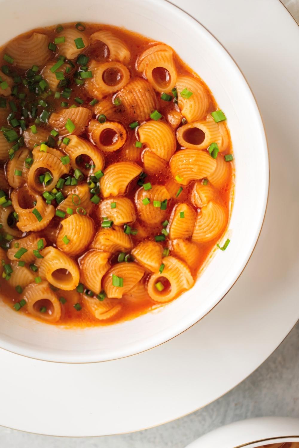 Sopa de conchas in part of a white bowl on top of a white plate.