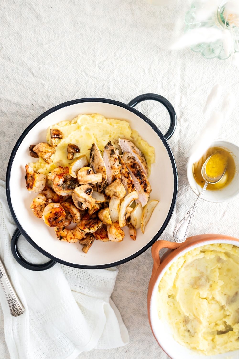 Mushrooms, grilled chicken, grilled shrimp, and potato purée in a white bowl. In front of the bowl is part of a white bowl that is filled with a potato purée.