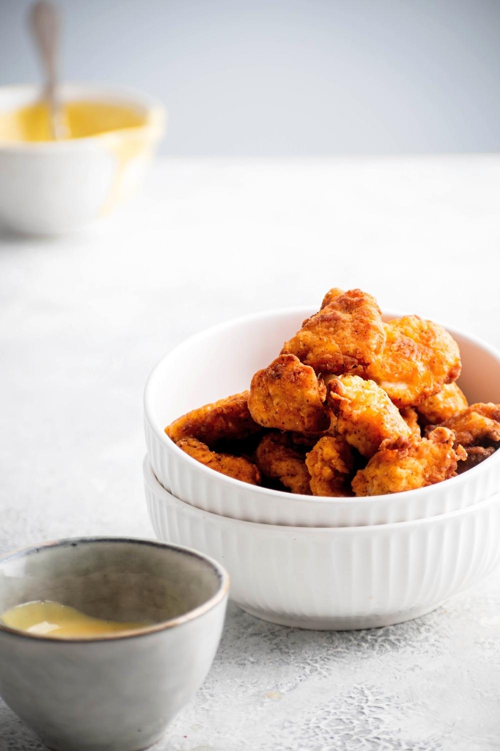 Chick-fil-A nuggets in a white bowl that is stacked on another white bowl. In front of it is a small gray bowl with Chick-fil-A sauce in it.