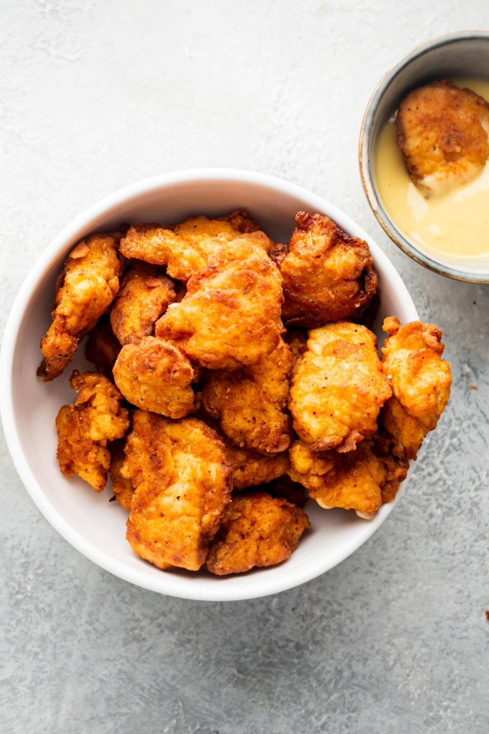 Chick-fil-A chicken nuggets in a white bowl. Next to it as part of a bowl of Chick-fil-A sauce with a chicken nugget in it.