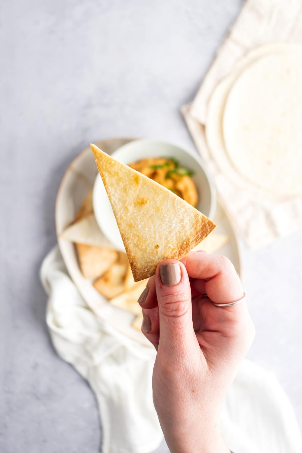 A hand holding one air fryer tortilla chip.