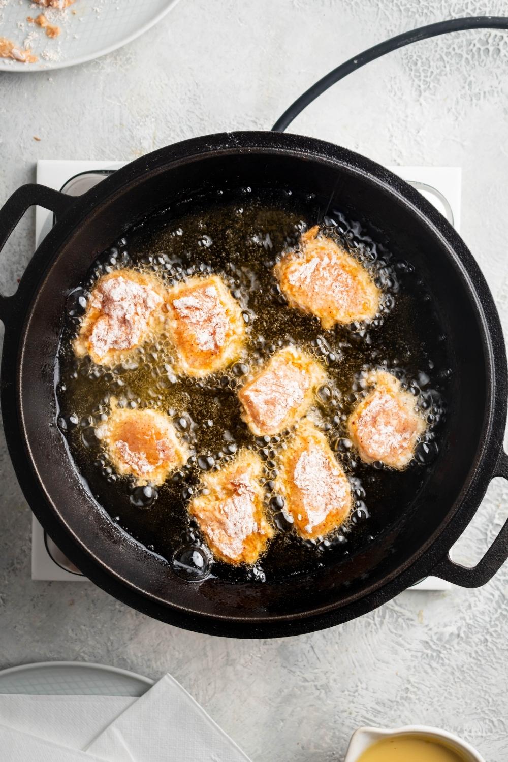 Eight pieces of breaded chicken frying in a pot with oil in it.