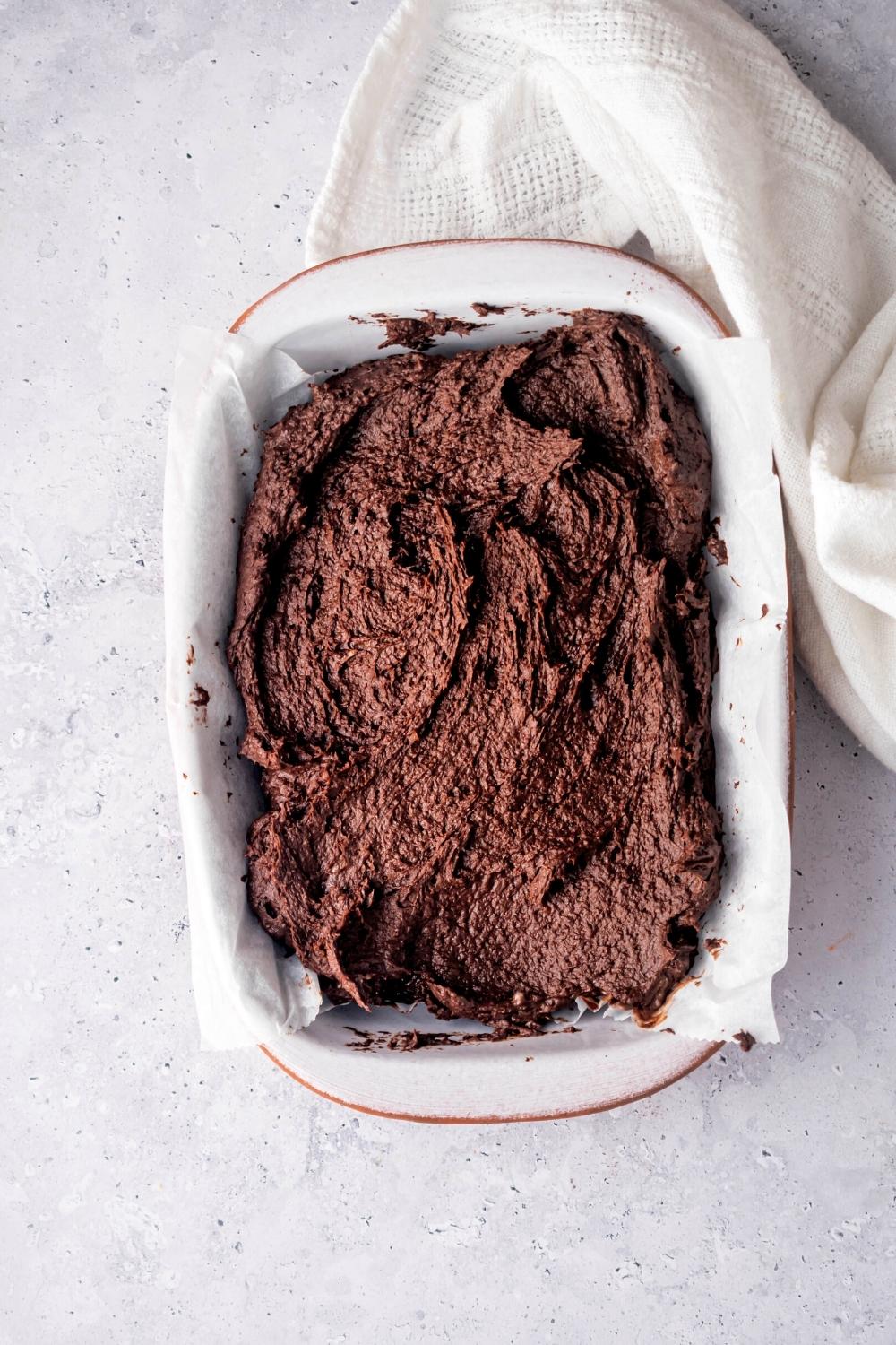 Brownie batter on top of a piece of parchment paper and a baking tray that is on a white counter.