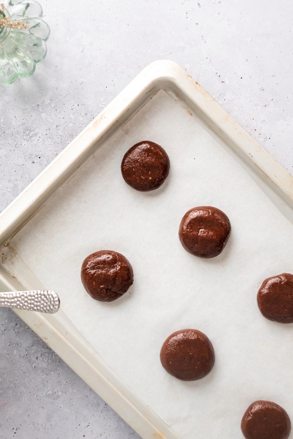 Three rows of three Nutella cookie dough balls on a piece of parchment paper on a baking sheet that is on a white counter.