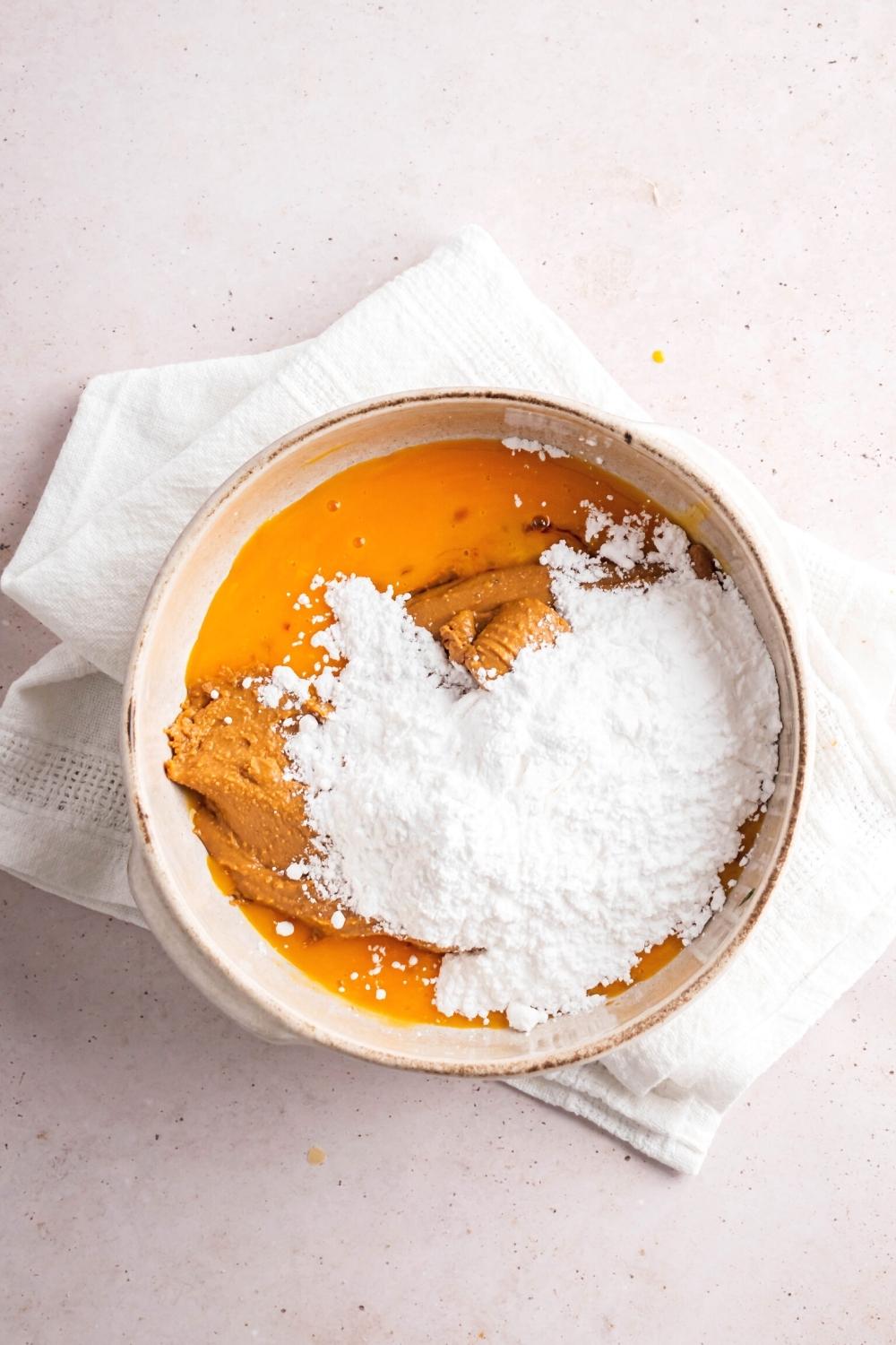 Confectioner erythritol, peanut butter, and egg yolk all in a white bowl on top of a white tablecloth on a white counter.