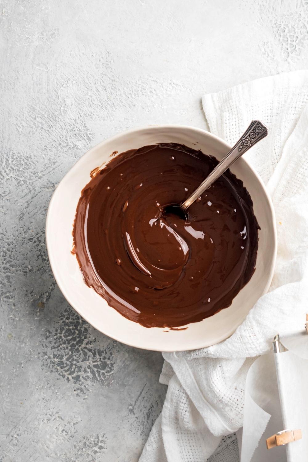 A bowl of melted chocolate chips and Nutella with a spoon in it.