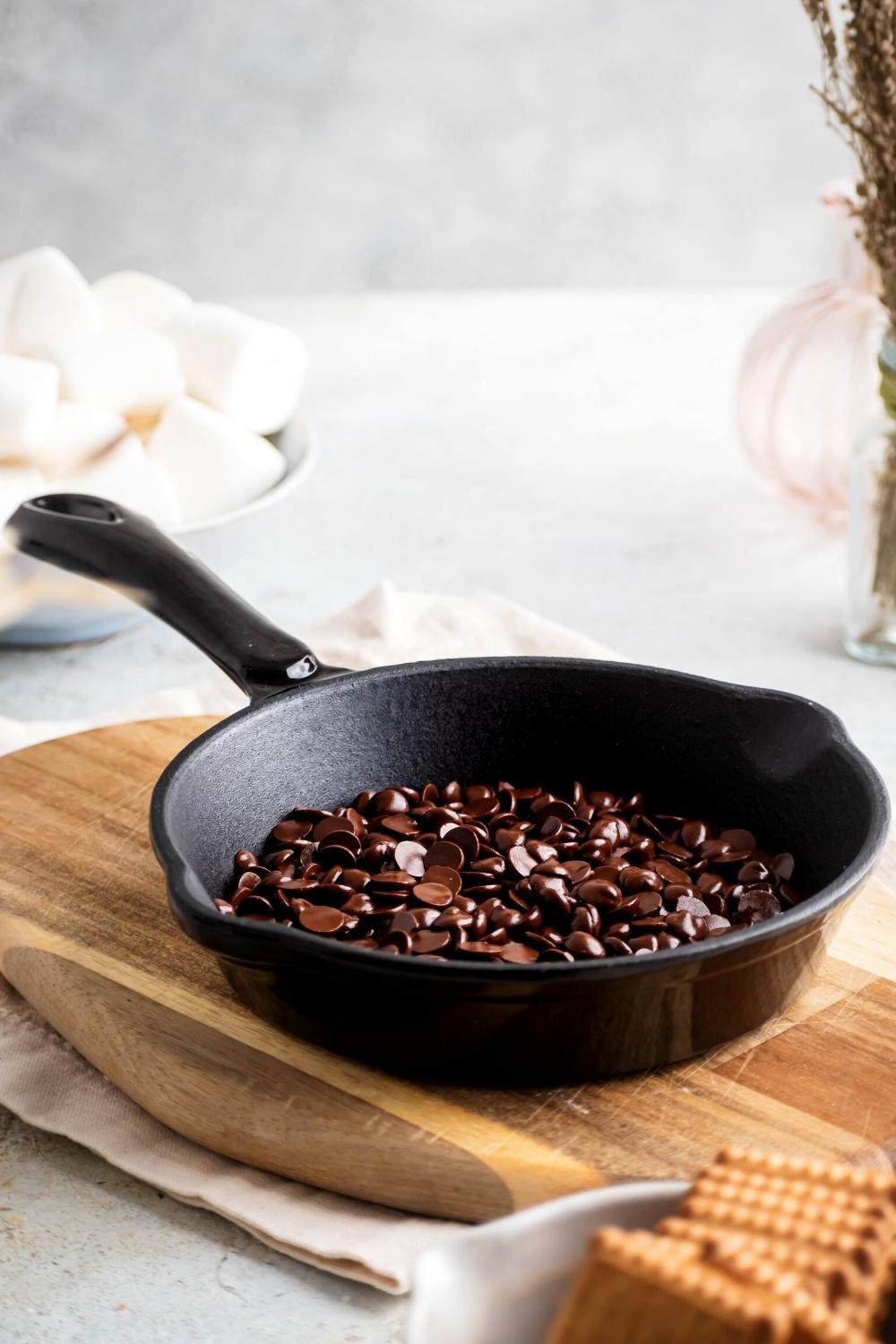 I partially melted chocolate chips in a cast iron skillet on top of a wooden cutting board on a white tablecloth on a white counter.