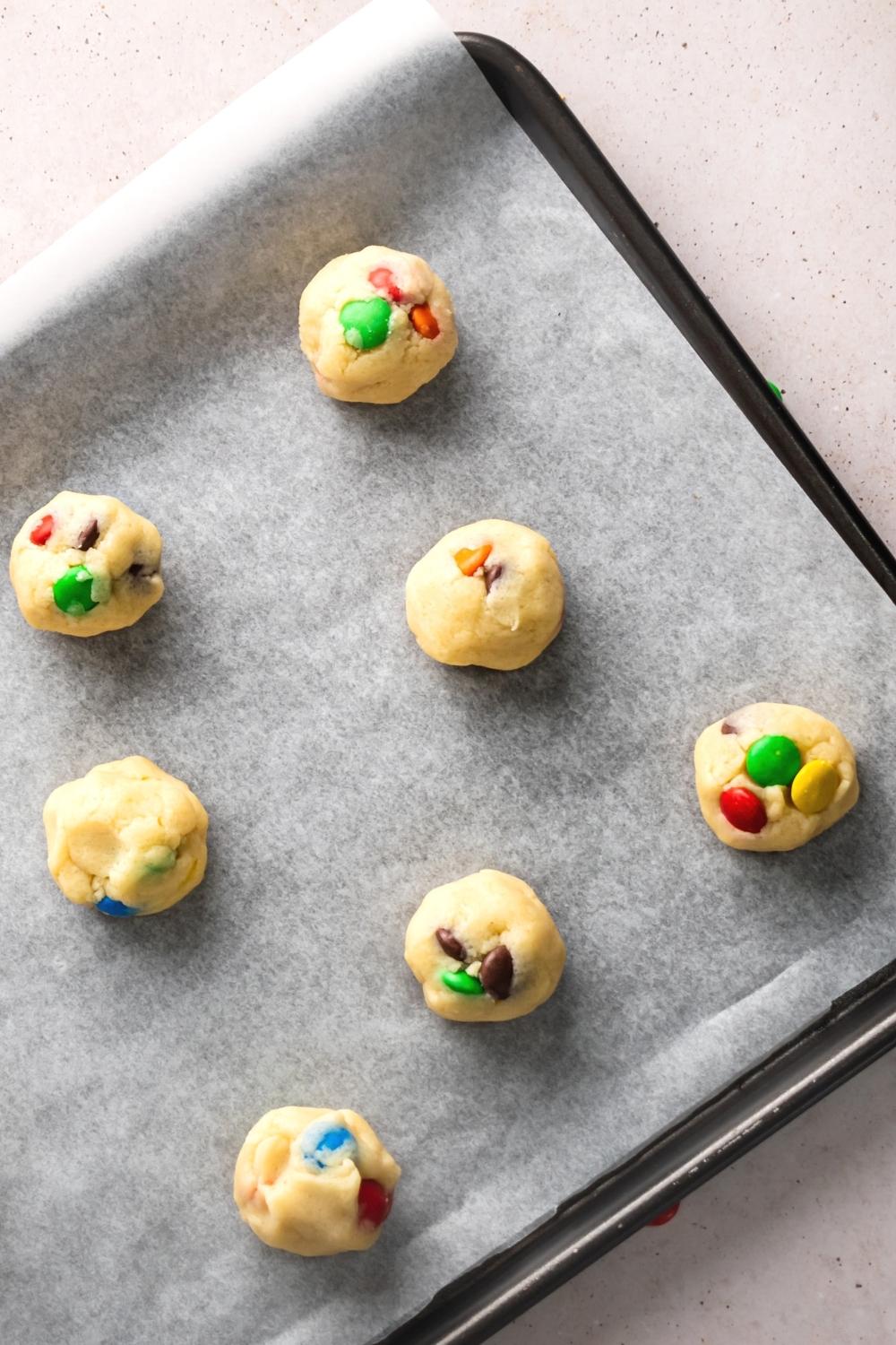 M&M cookie dough balls on a sheet of parchment paper on a baking tray.