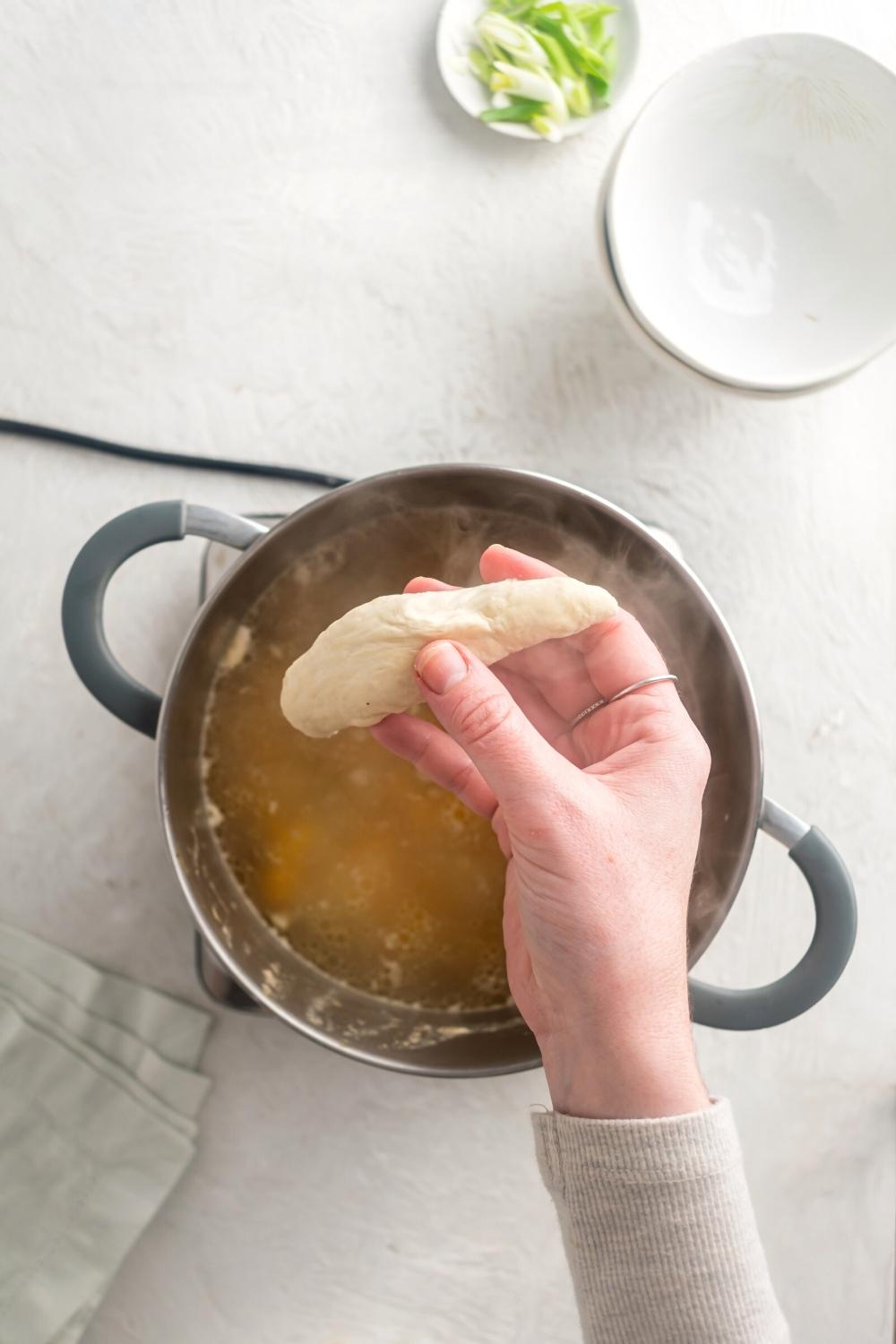 A hand holding a dumpling over a pot filled with Jamaican chicken soup.