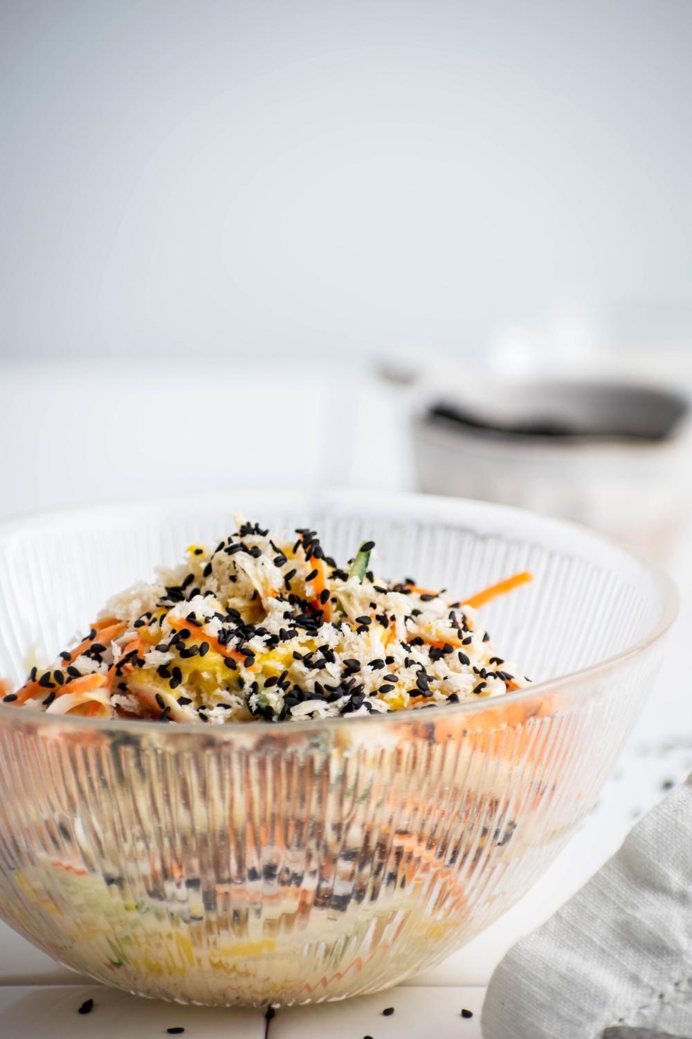 A glass bowl filled with kani salad with black sesame seeds on top.