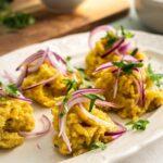 Five clumps of mangu with pickled red onion on top of it on a white plate.