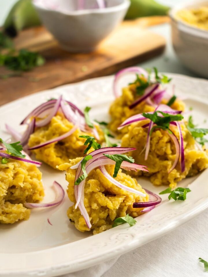 Five clumps of mangu with pickled red onion on top of it on a white plate.