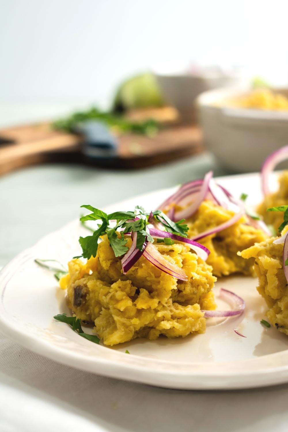 A scoop of mangu with slices of red onion and parsley on top of it on a white plate.