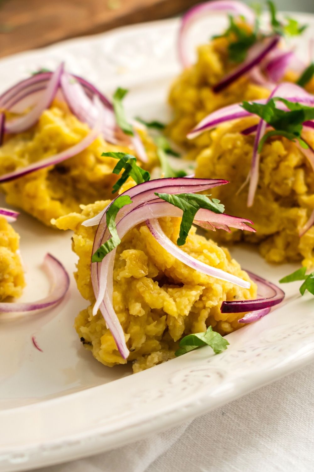 A ball of mangu with picked red onion on top of it on a white plate with more mangu on it.