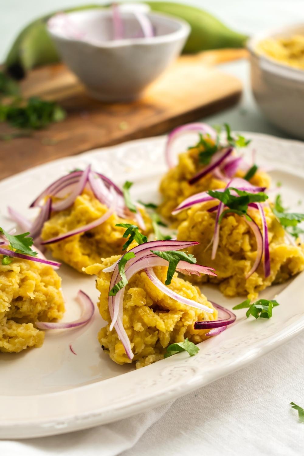 Five clumps of mangu with pickled red onion on top of it on a white plate.