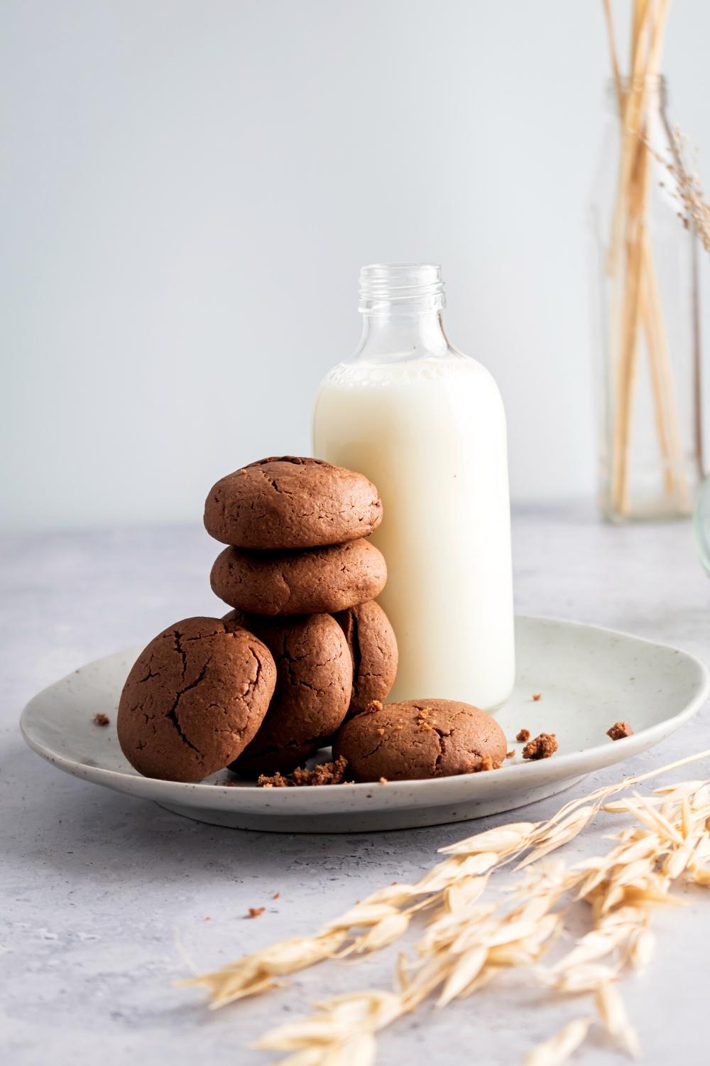 Six Nutella cookies on a plate stacked and overlapping one another leaning against a glass bottle of milk.