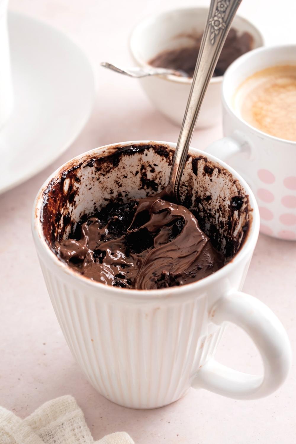 A white mug filled with a Nutella mug cake with a spoon in it.