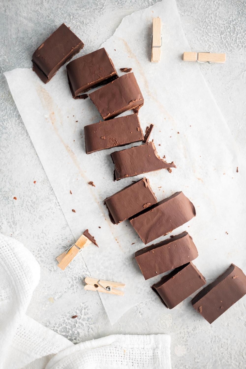 A diagonal line of ten pieces of fudge on a sheet of parchment paper on a white counter.