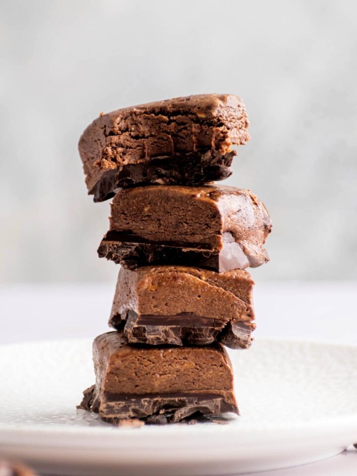 A stack of four protein brownies on a white plate. The top brownies has a bite out of the front of it.