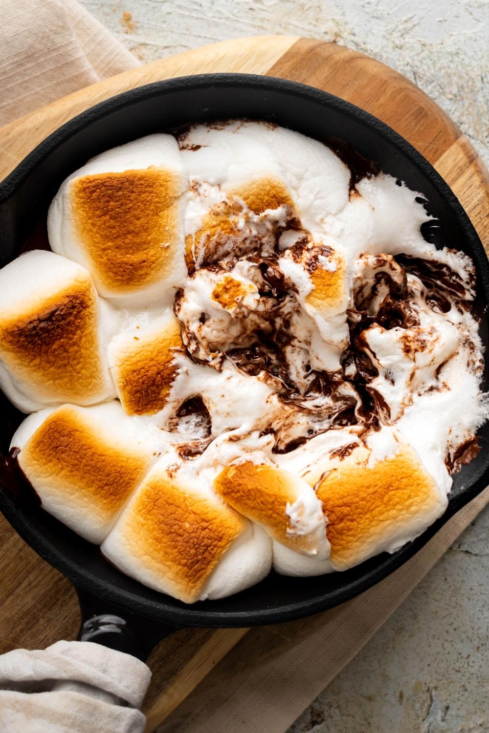 Golden marshmallows in a cast-iron skillet with some of them smashed and melted chocolate showing.