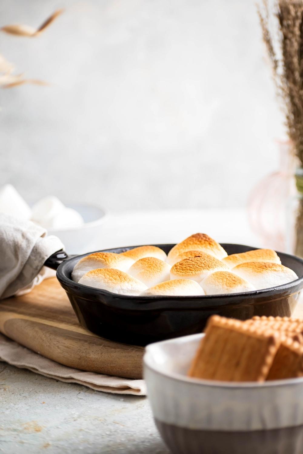 S'mores dip in a cast iron skillet on top of a wooden cutting board.