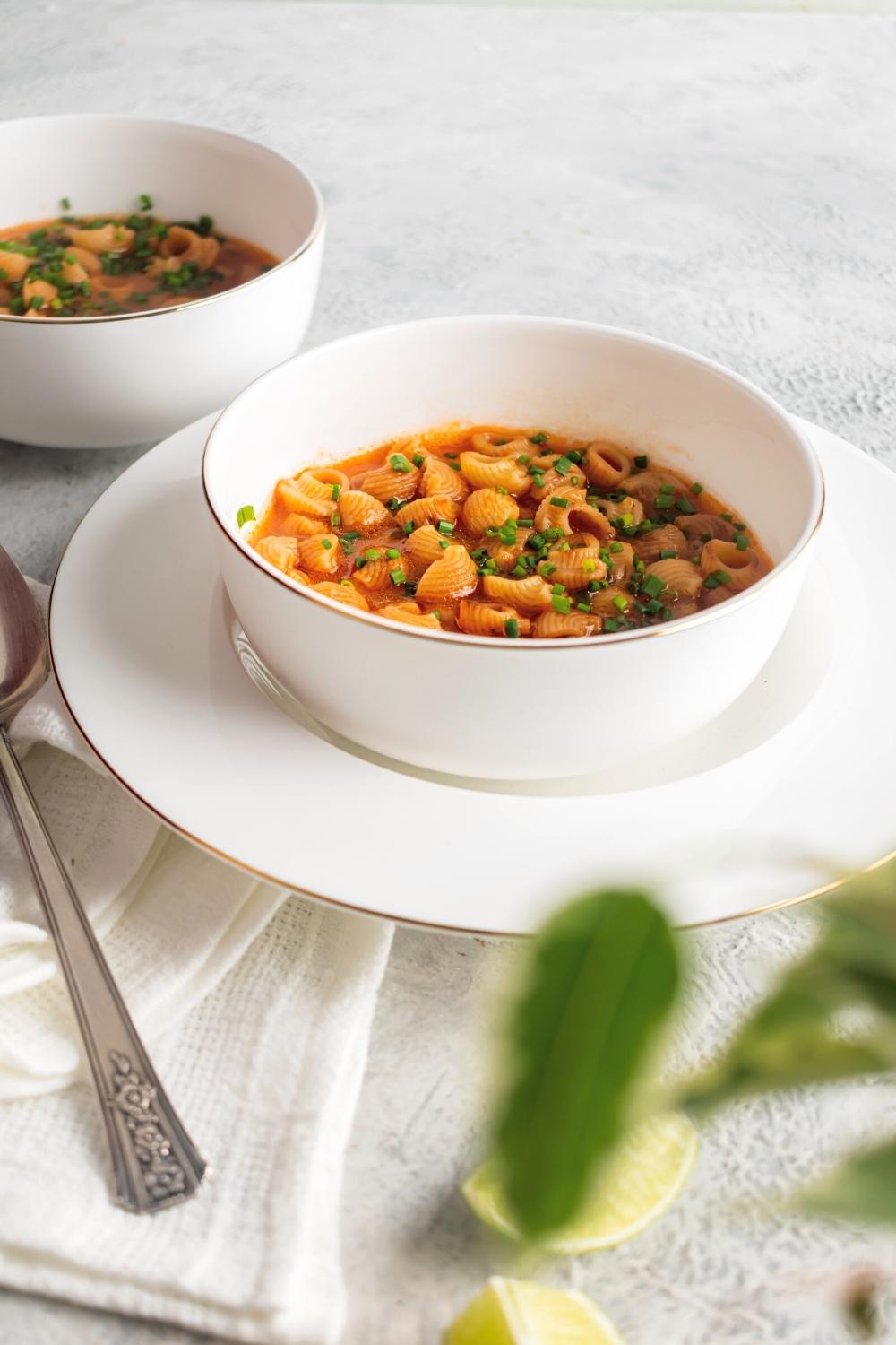 Sopa de conchas in a white bowl on top of a white plate. Behind it is part of a white bowl filled with the soup.