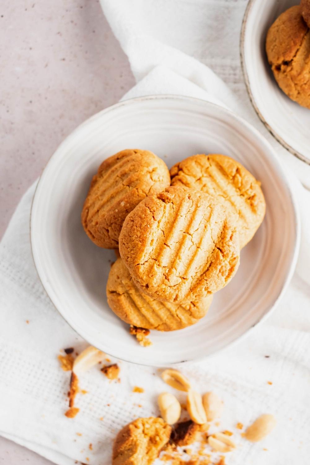 A peanut butter cookie on top of three more peanut butter cookies on top of a white plate on a white tablecloth.