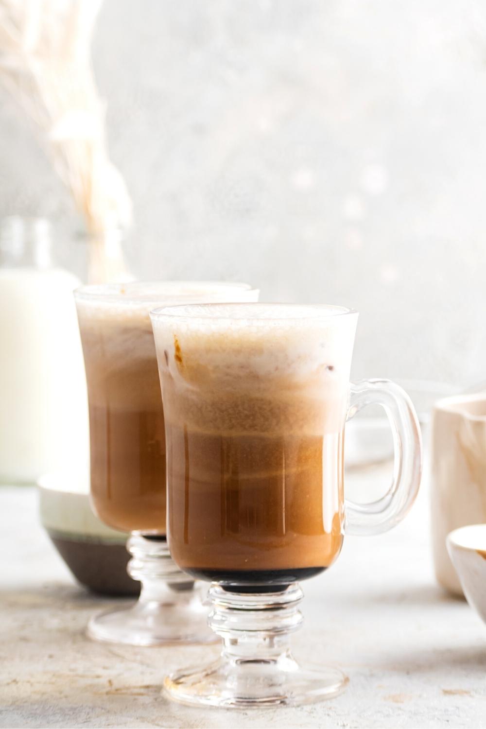 A glass mug that is filled with salted caramel cream cold brew with another glass mug filled with the cold brew behind it.