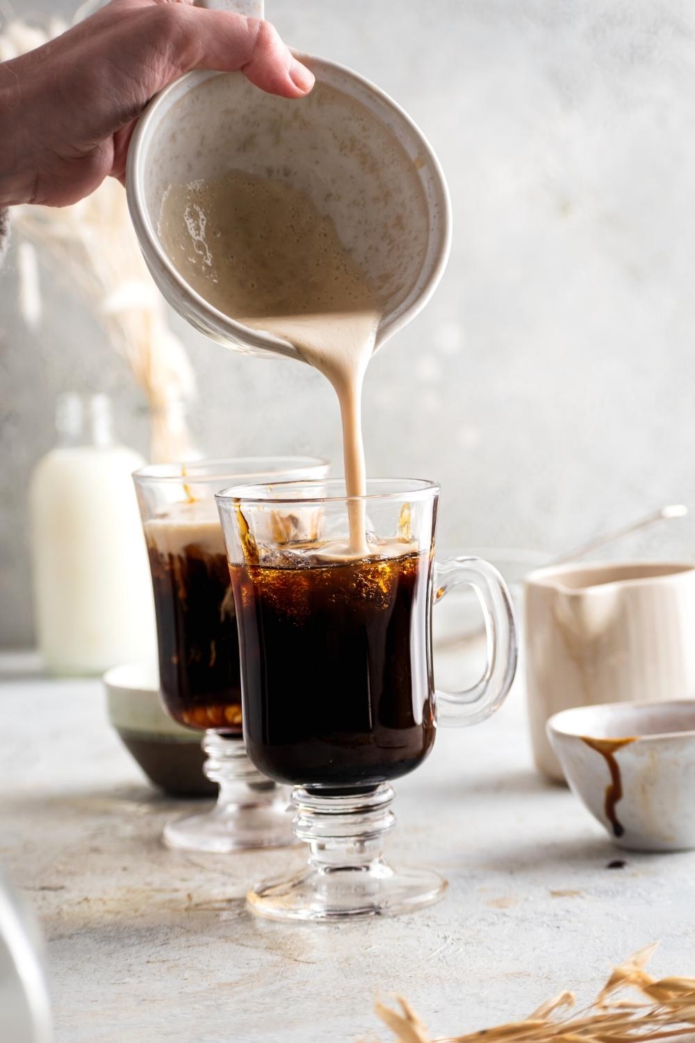 A hand pouring caramel cold foam on top of cold brew coffee in a glass cup.