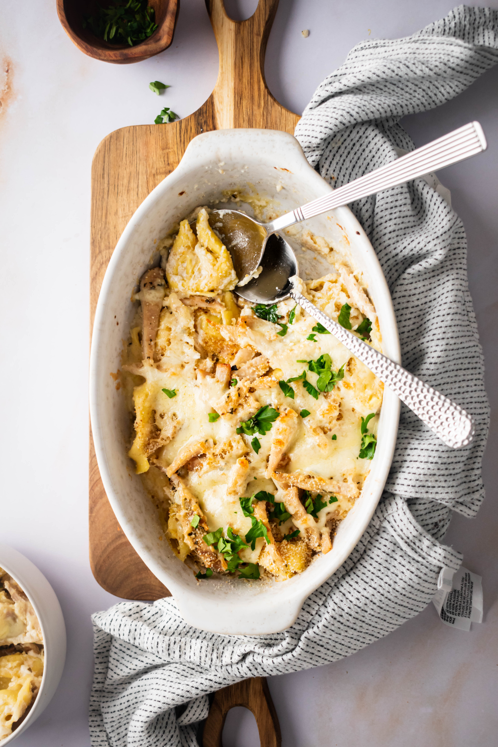 Teaspoons in a baking dish that is filled with Olive Garden asiago tortellini Alfredo with grilled chicken.