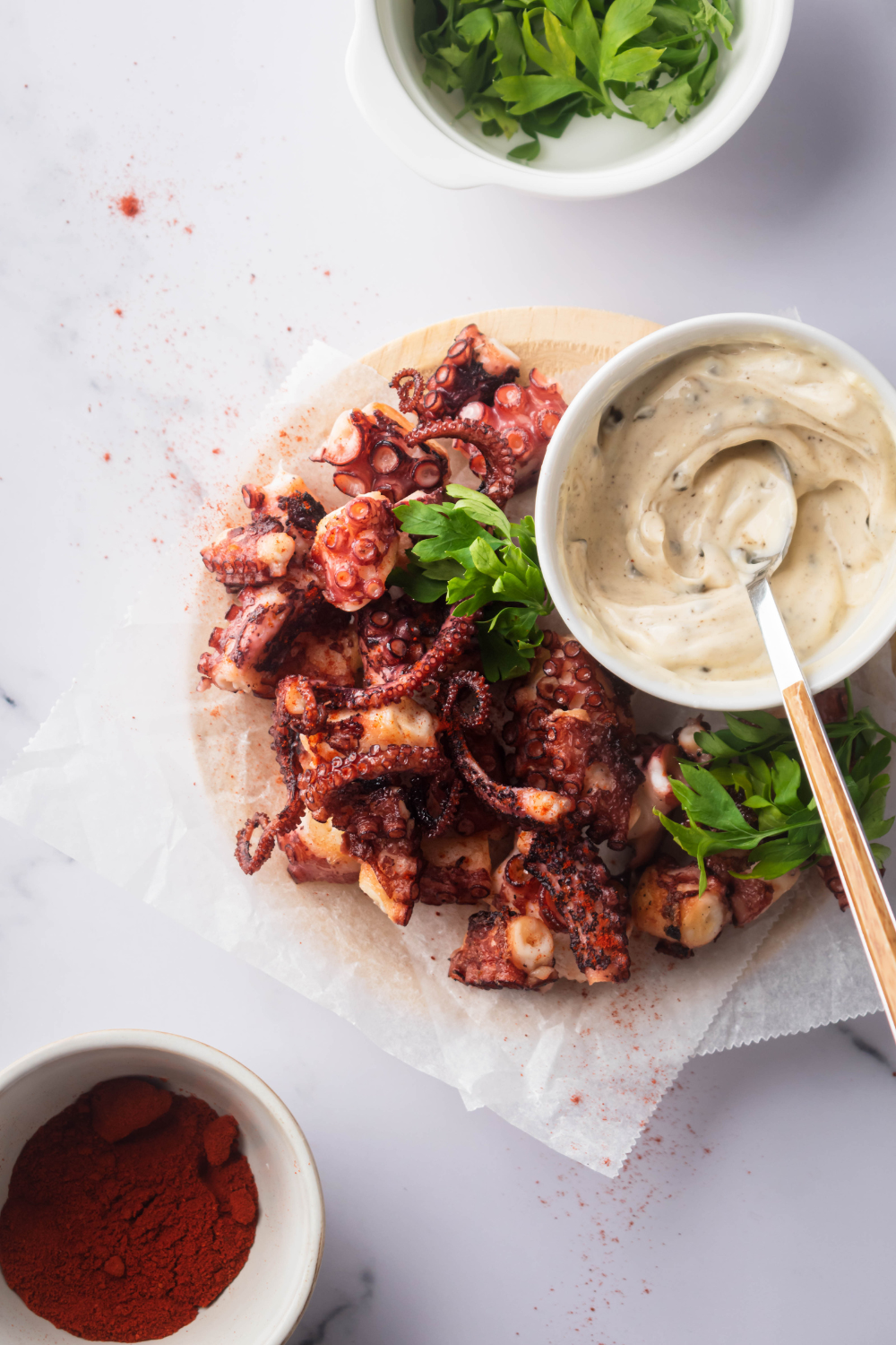 Fried octopus on sheets of parchment paper on a plate that has a bowl of male dipping sauce on it.