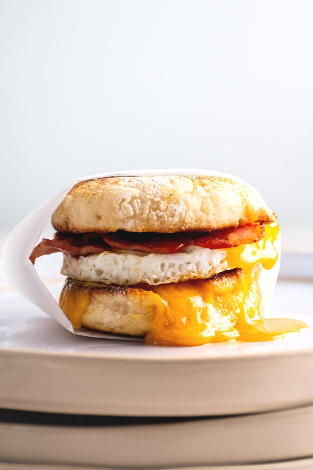 A mcdondals egg mcmuffin wrapped in parchment paper on a white plate.