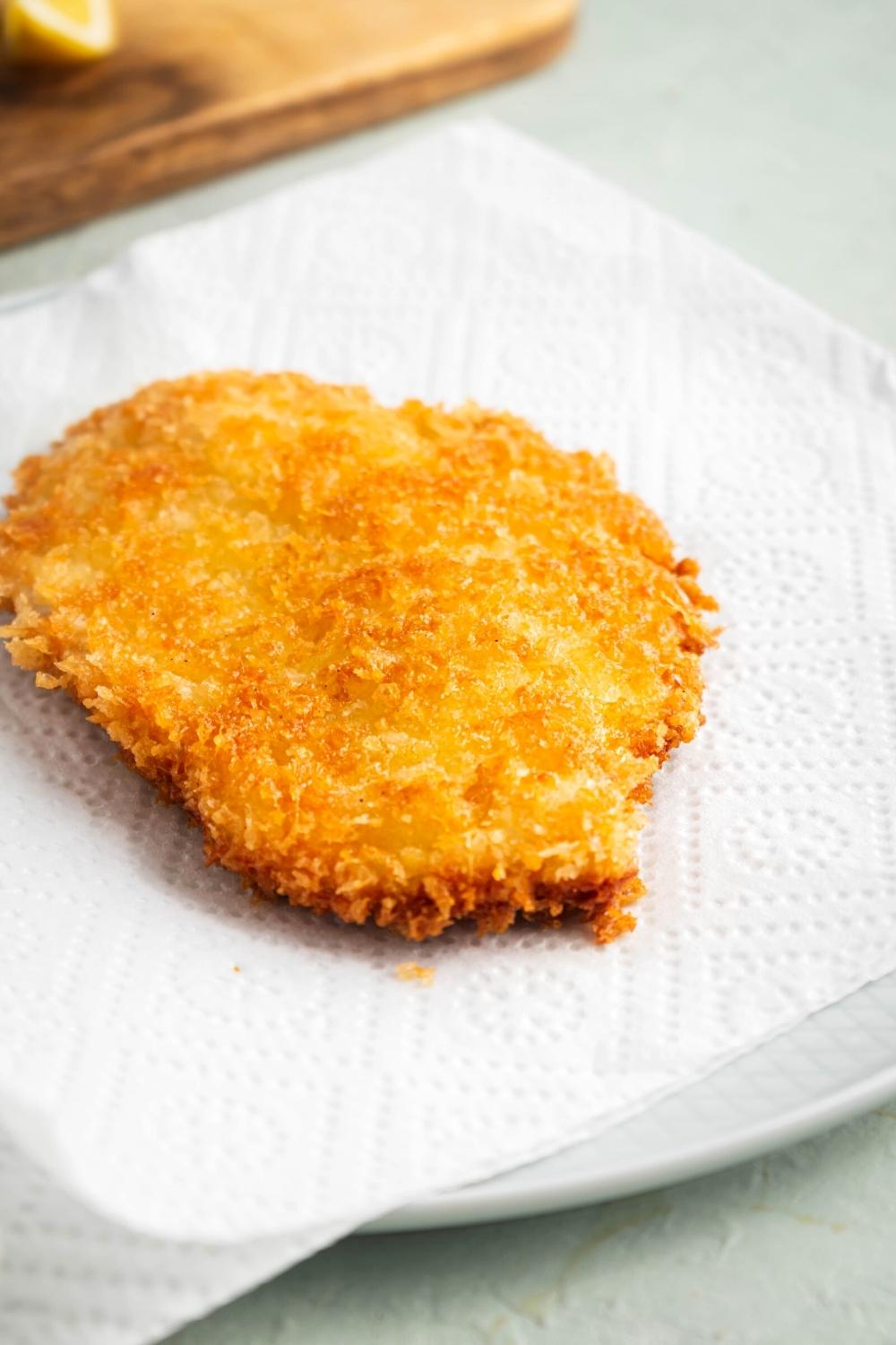 A chicken cutlet on a paper towel lined plate.