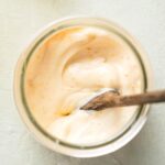 Wooden spoon submerged in chipotle mayo that is in a glass jar.