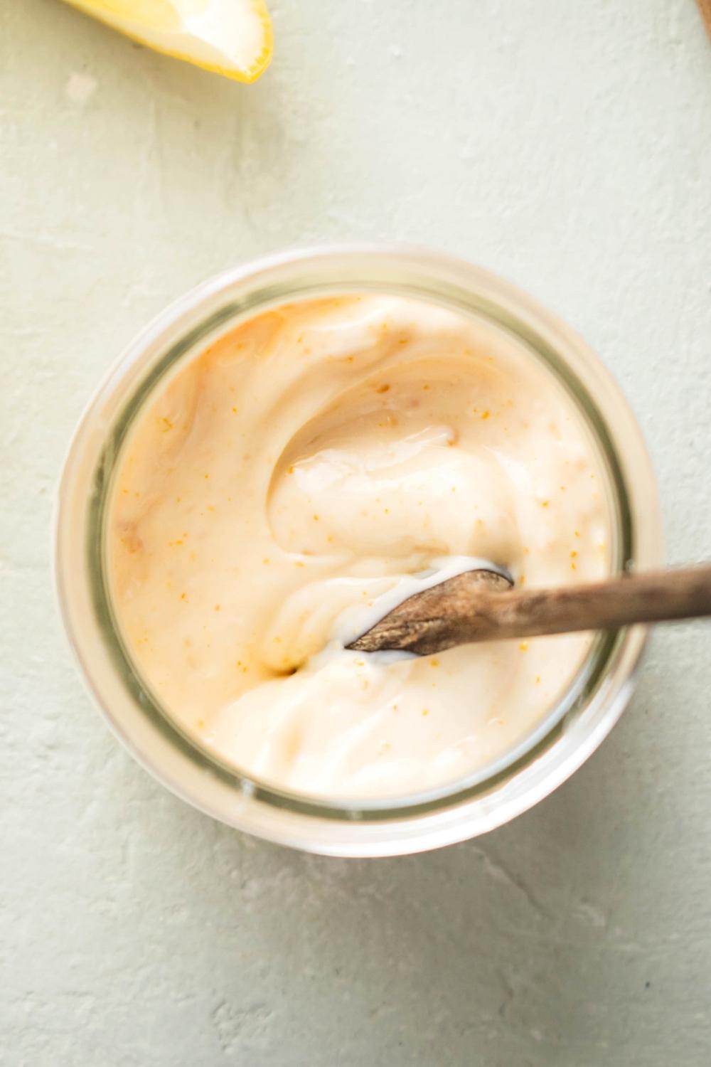 Wooden spoon submerged in chipotle mayo that is in a glass jar.