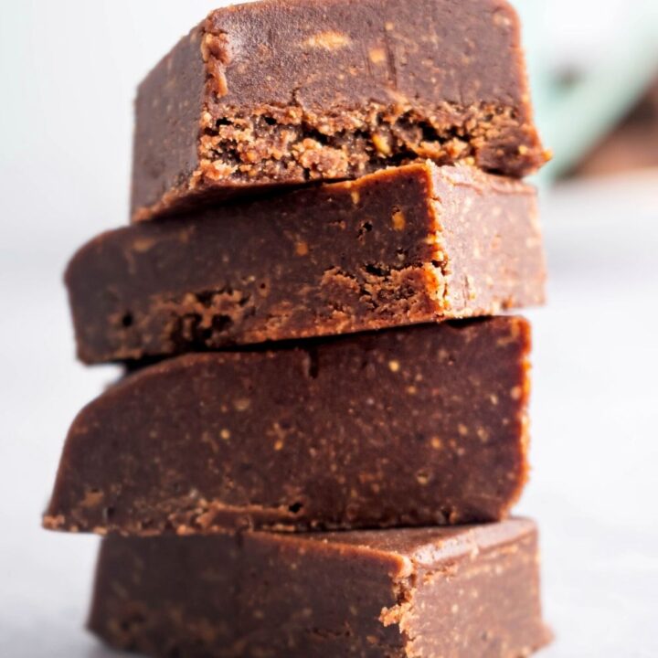 Four pieces of chocolate peanut butter fudge staggered on top of one another on a white counter.