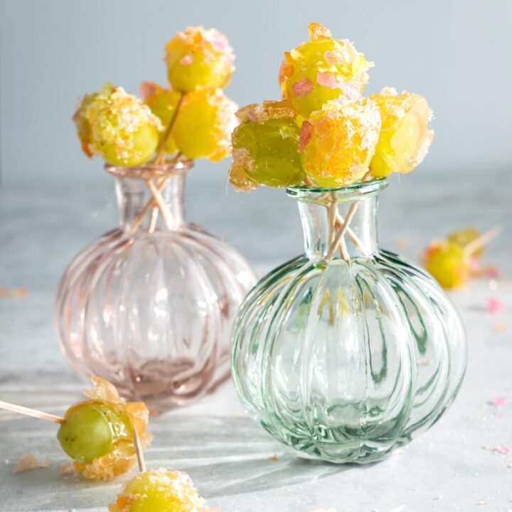 Two glass vases that have crack grapes with toothpicks in certain in them in the base. Surrounding the base are some of the crack grapes