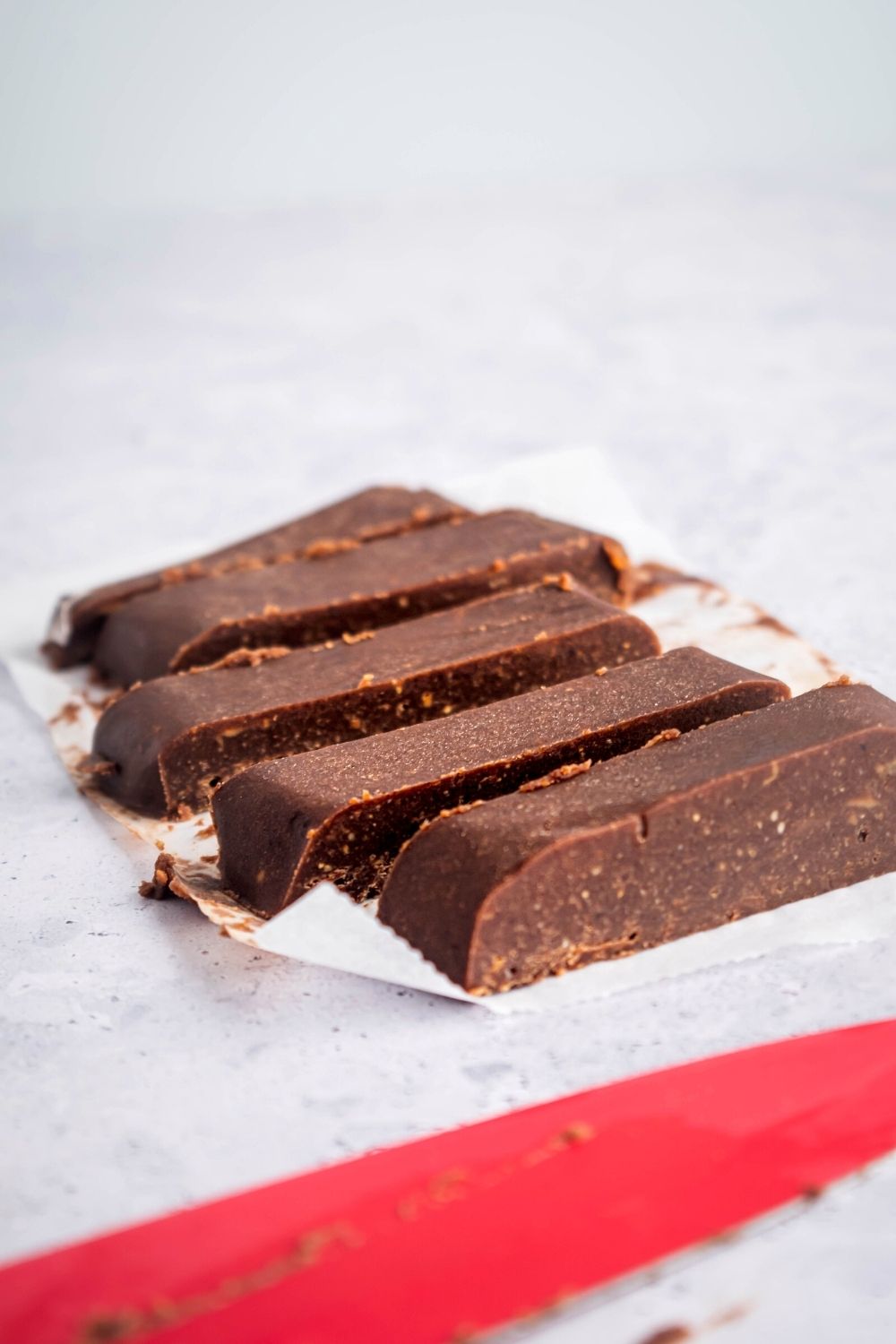 Five strips of peanut butter chocolate fudge on a piece of parchment paper on a gray counter.