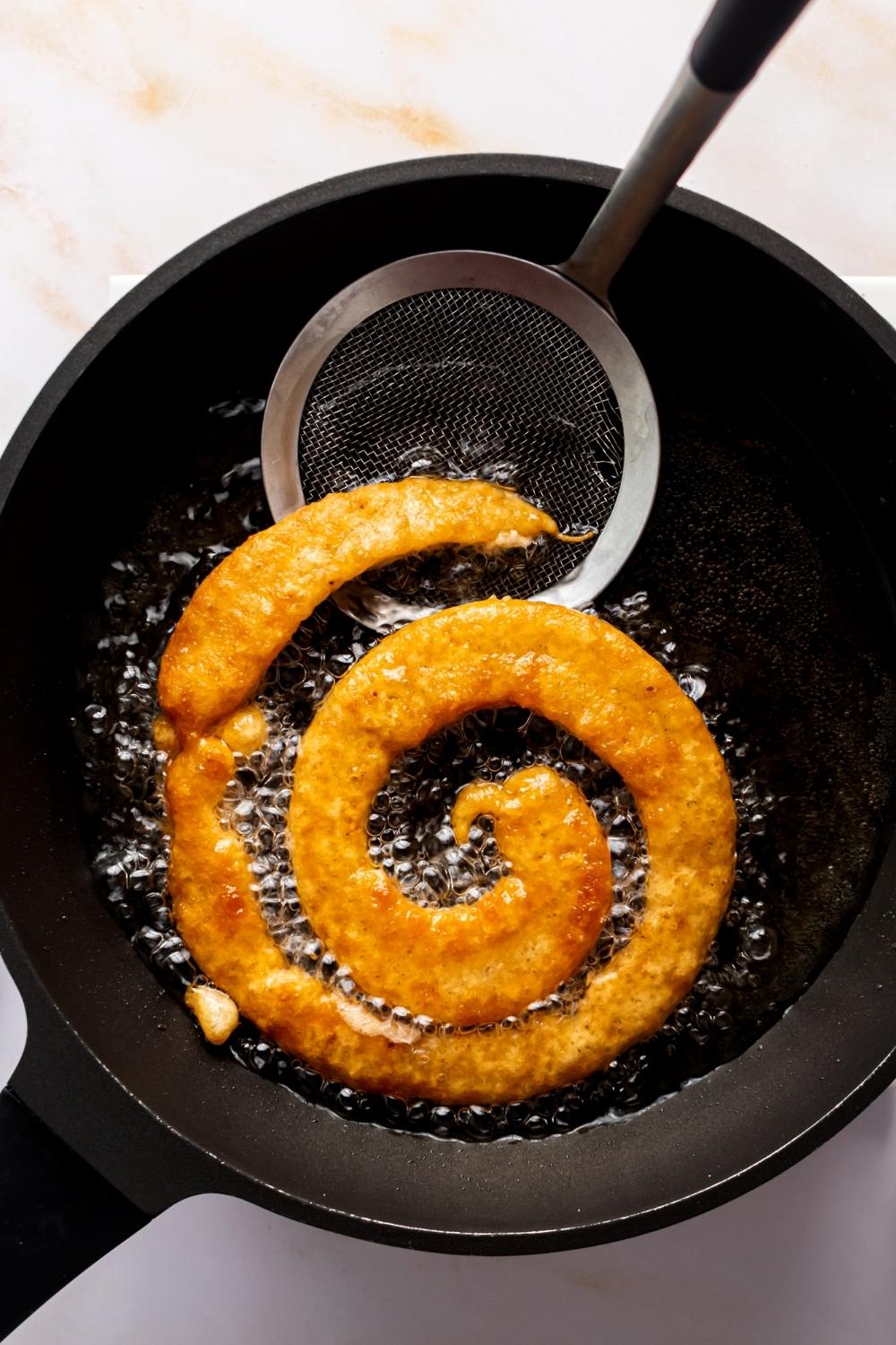 A fried funnel cake in a a pan that is filled with oil.
