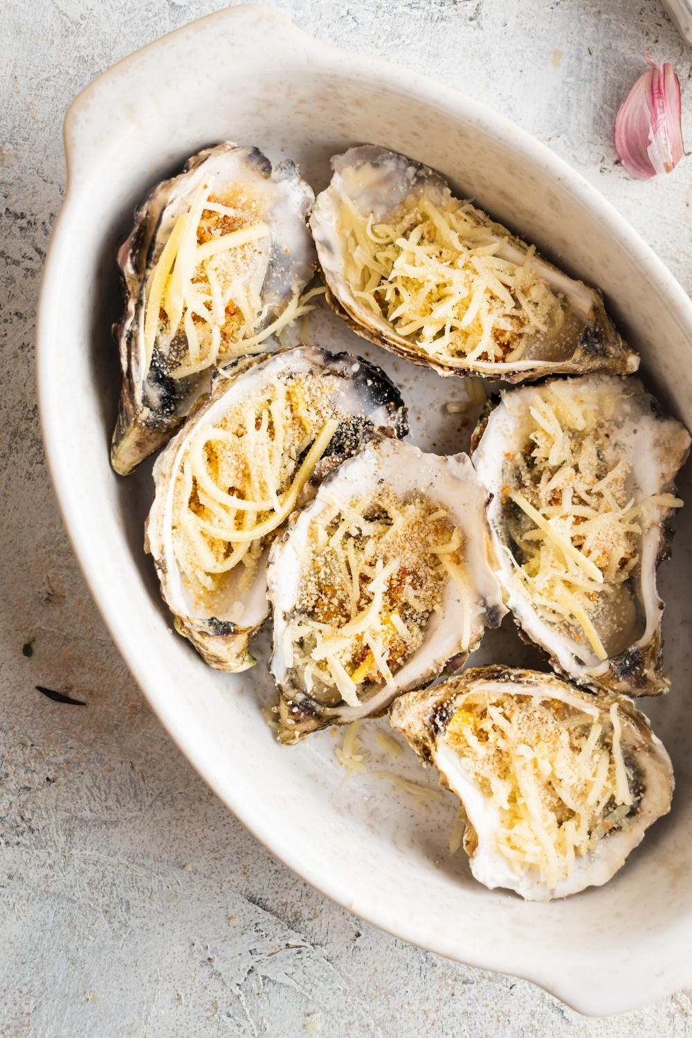 Mozzarella cheese and breacrumbs in six oysters in a baking dish.