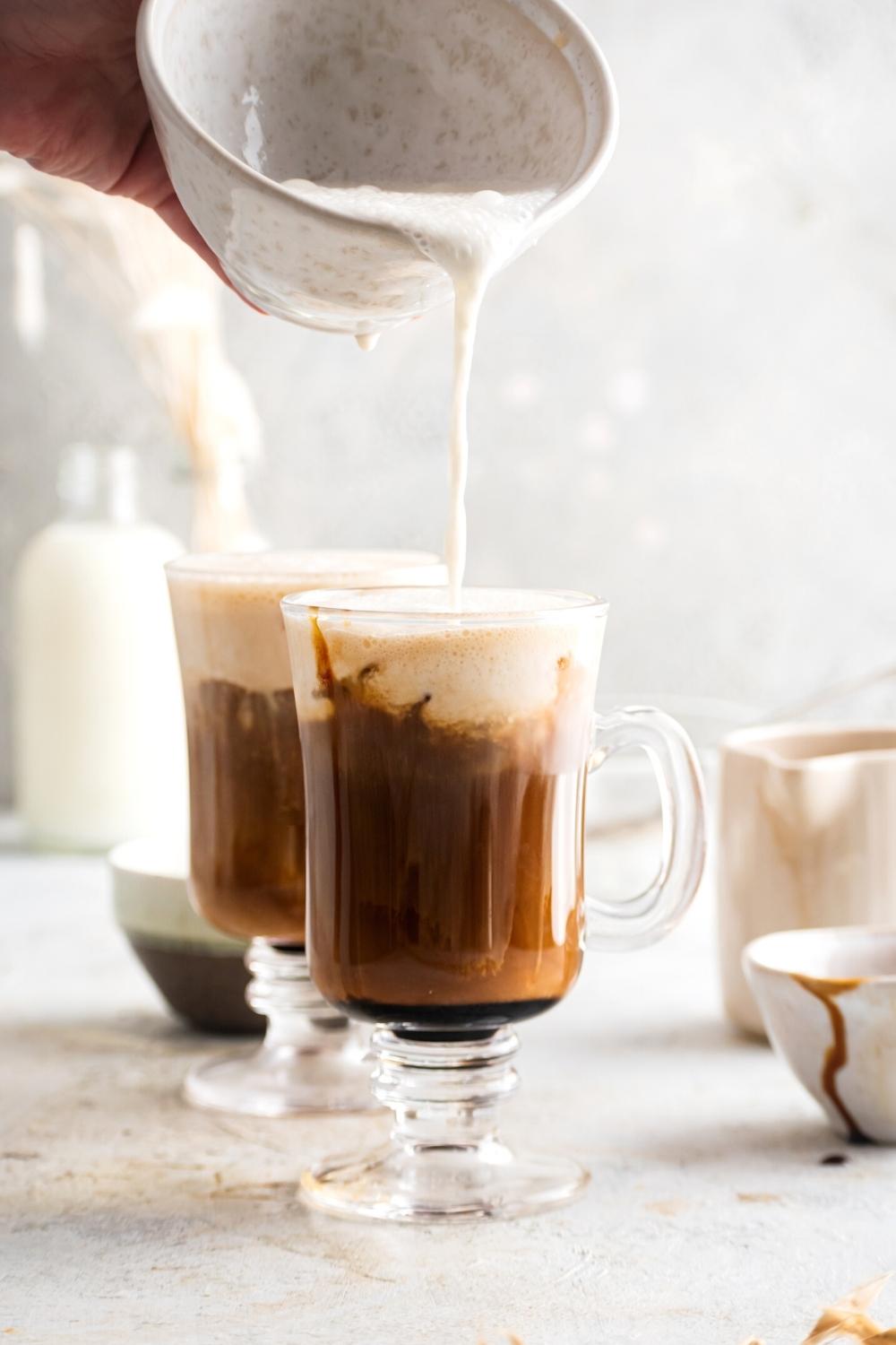 A hand pouring caramel cream cold foam into a glass that is filled with cold brew.