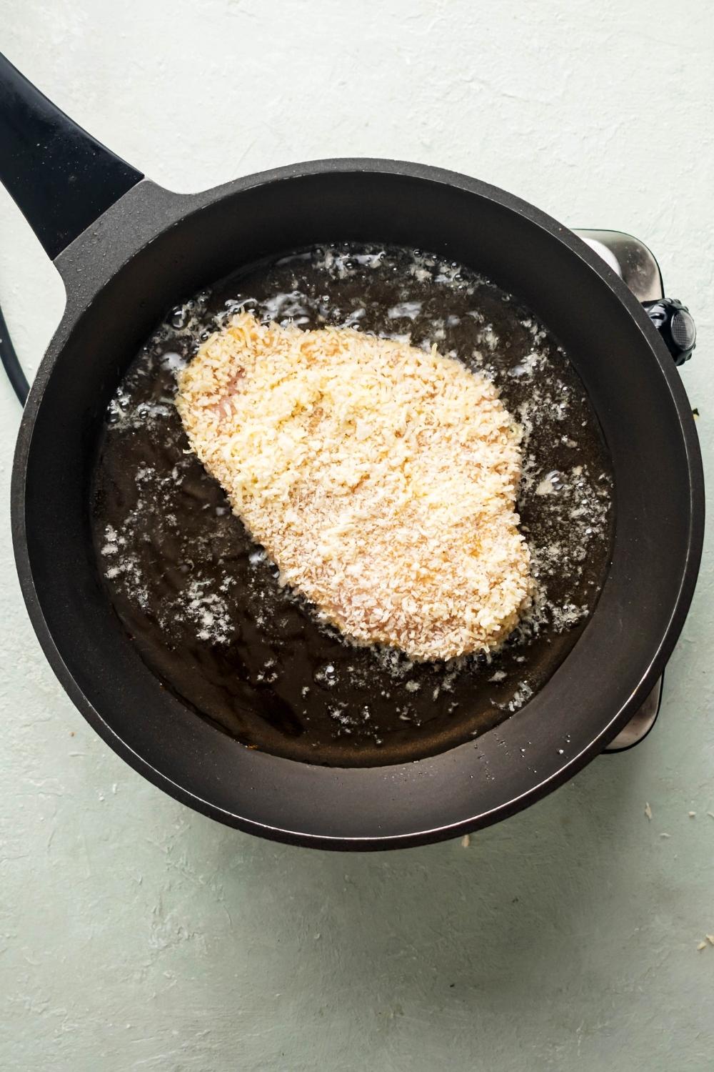 A breaded chicken cutlet in oil in a pan.