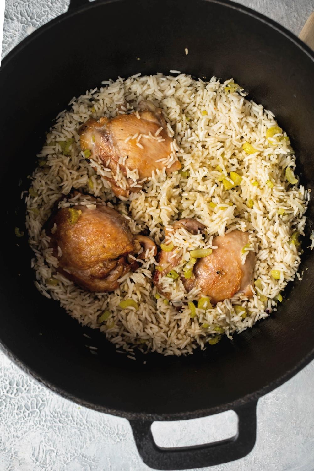 Chicken thighs and white rice in a Dutch oven.