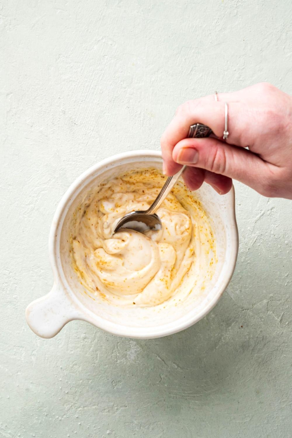 Hand holding a spoon mixing chipotle mayo and a white boulders on a white counter.