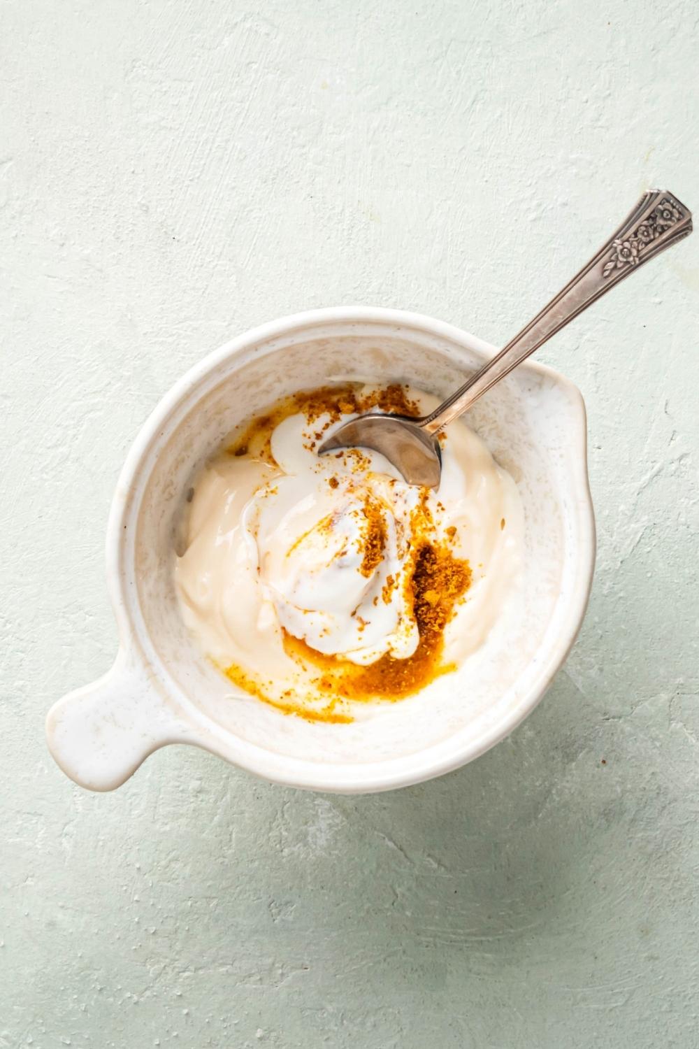 Chipotle mayo ingredients in a silver spoon and a white ball on a white counter.