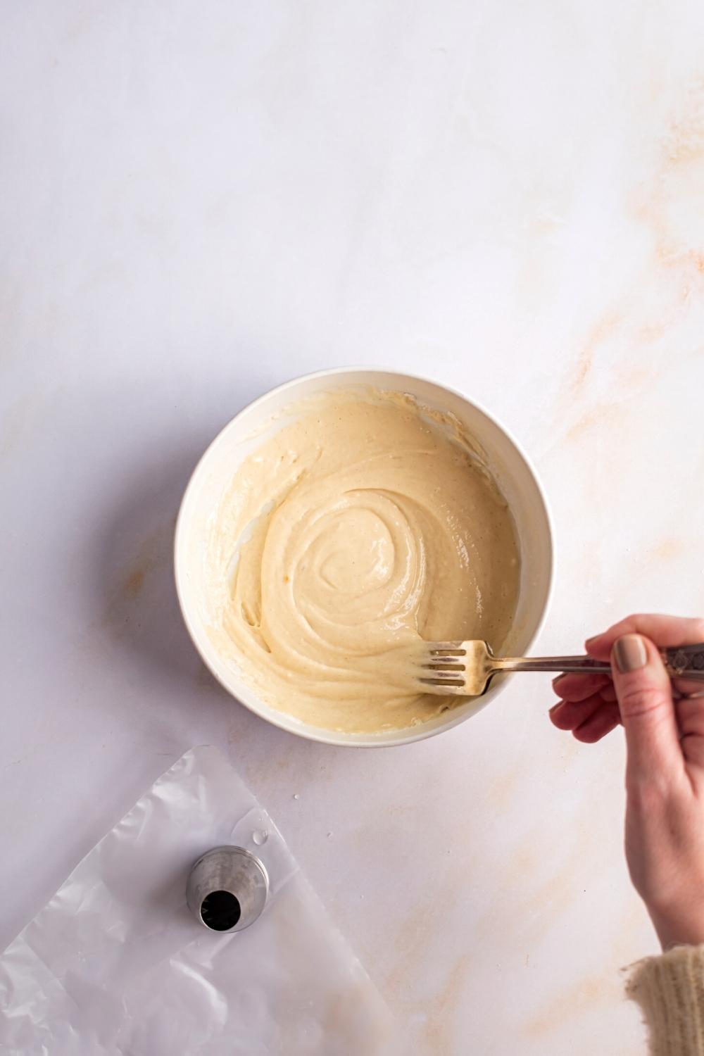 A hand holding a fork mixing funnel cake made with pancake mix in a bowl.