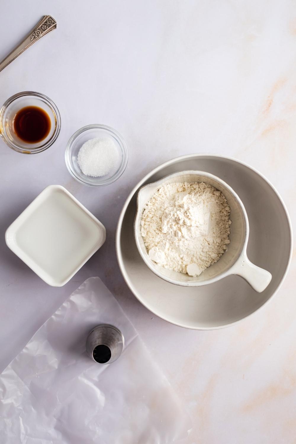 A bowl of pancake mix, a bowl water, a bowl of salt, and a bowl of vanilla extract all on a white counter.