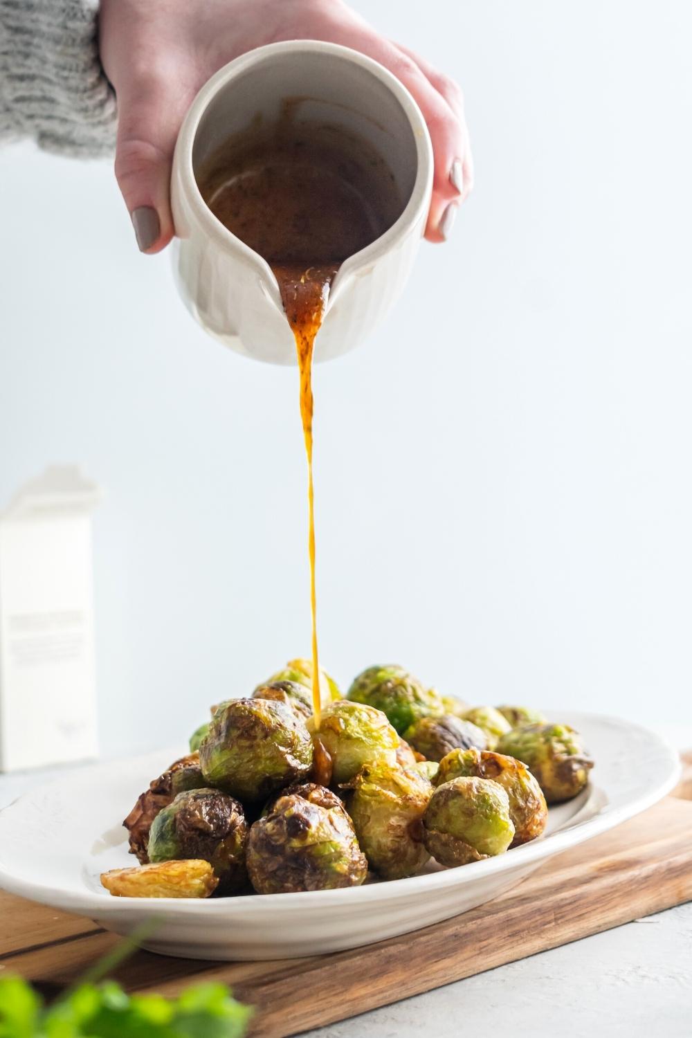 A hand holding a pitcher drizzling honey on top of brussel sprouts on a plate.