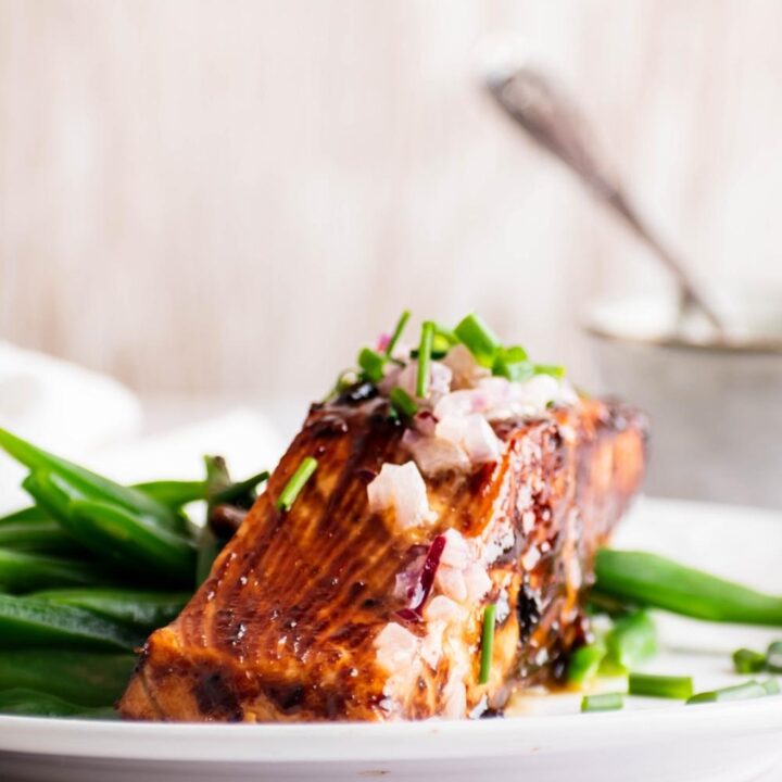 A piece of miso salmon with snow peas on a white plate.